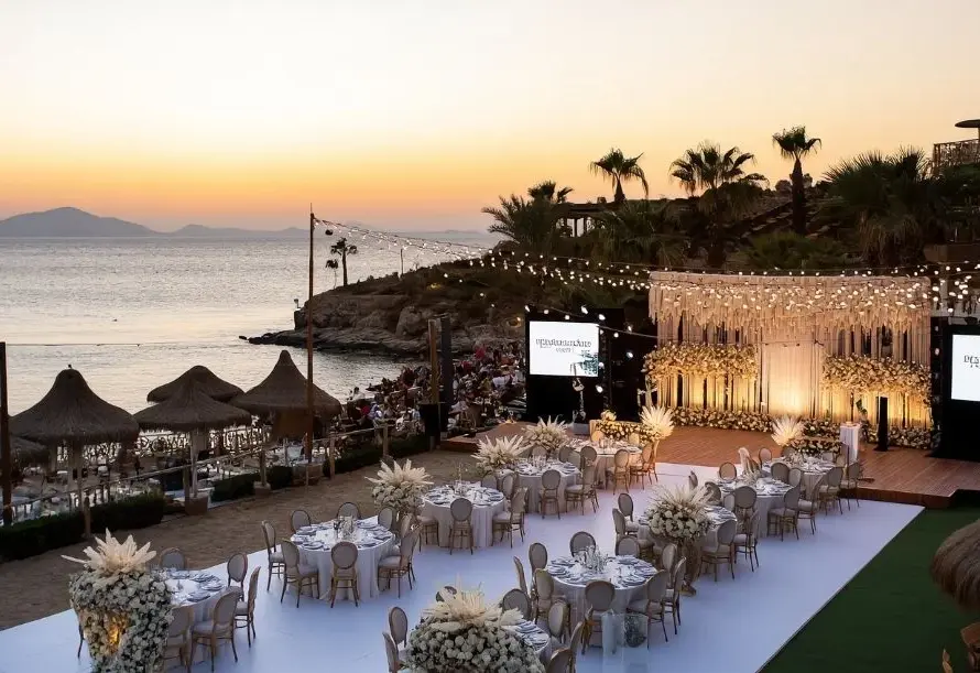 Beachfront corporate event setup with elegant table arrangements and stage decoration at sunset in Bodrum, Turkey