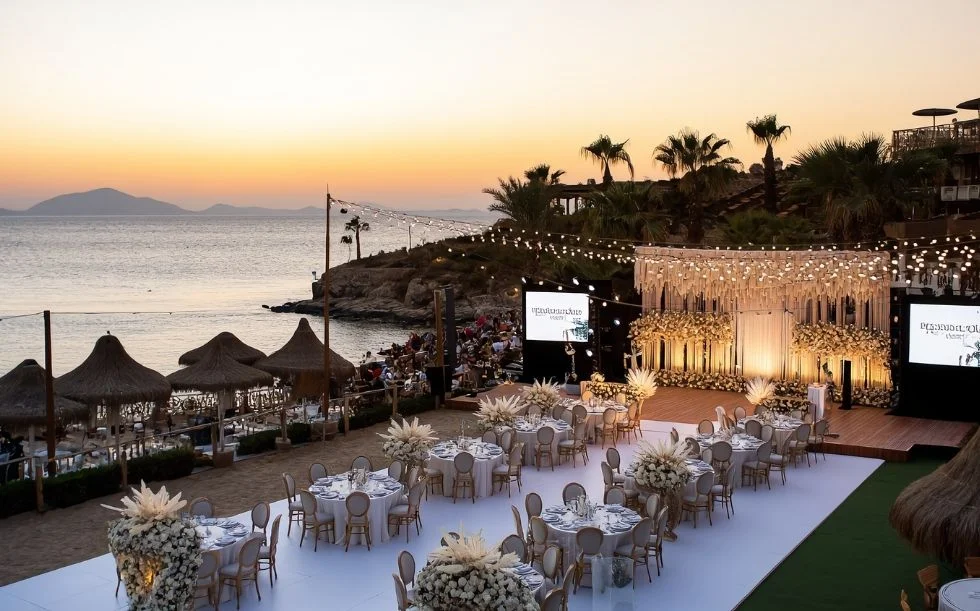 Beachfront corporate event setup with elegant table arrangements and stage decoration at sunset in Bodrum, Turkey